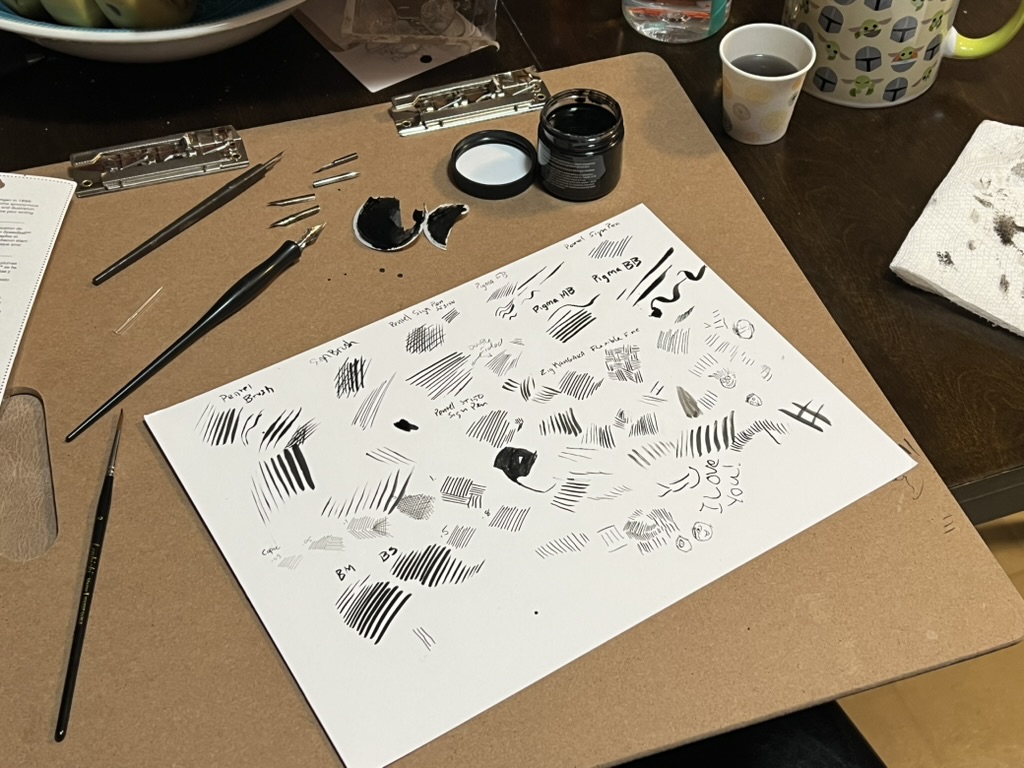 A drawing board holds bristol board paper with black lines and curves of ink tests.