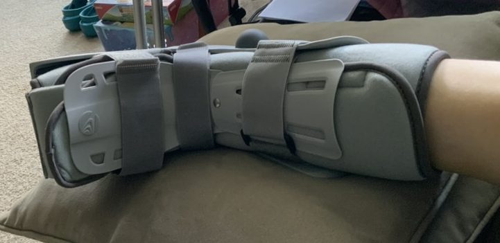 A foot in an air cast walking boot resting on a stack of throw pillows.